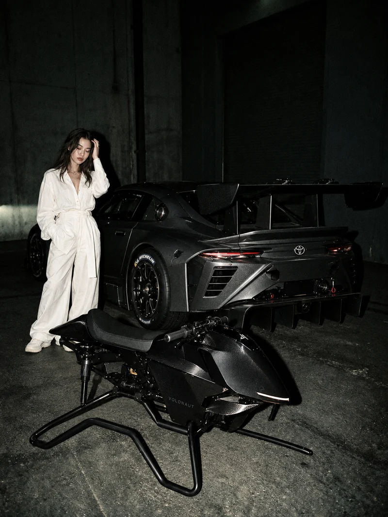 Worth a Shot fictional editorial: a model, black Toyota GR GT3 and Volonaut airbike in a flash-lit garage